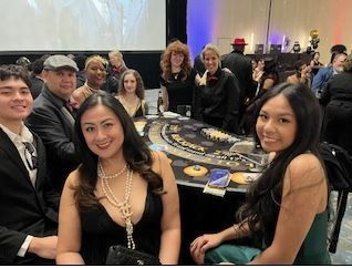 A group of people dressed in formal attire gather around a gaming table at a party.