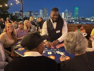 Dealer dealing cards at an outdoor casino table at night, with city lights in the background