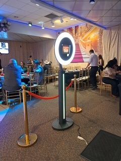 Indoor event space with people seated at tables, a glowing photo booth, and blue accent lighting