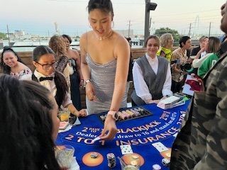 People gathered around a blue tabletop game at an outdoor event, with one woman reaching to place a piece.