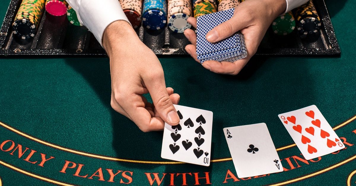 A dealer's hands place playing cards on a green table with stacks of colorful chips arranged nearby.