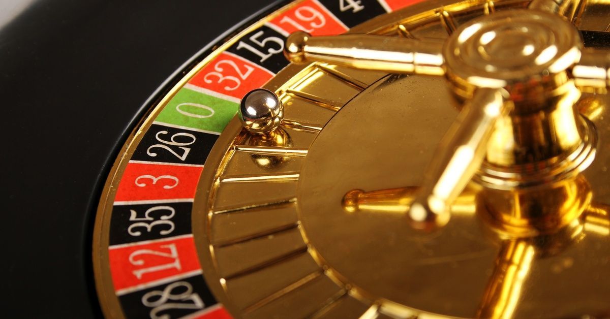 Close-up of a gold roulette wheel. It features a silver ball that moves between numbered red, black, and green spaces.