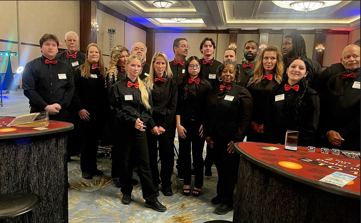 A group of people wearing black shirts and red bow ties stand together in a hotel banquet room.