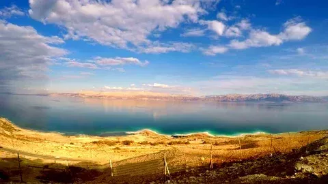 Panoramic coastal landscape with blue sea, golden hills, and a cloudy sky at sunset
