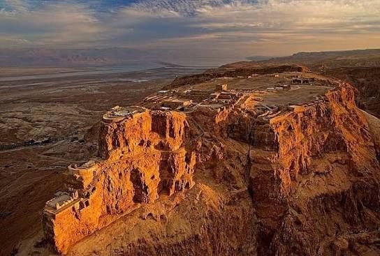 Sunlit red-orange canyon cliffs overlooking a vast desert plain at sunset