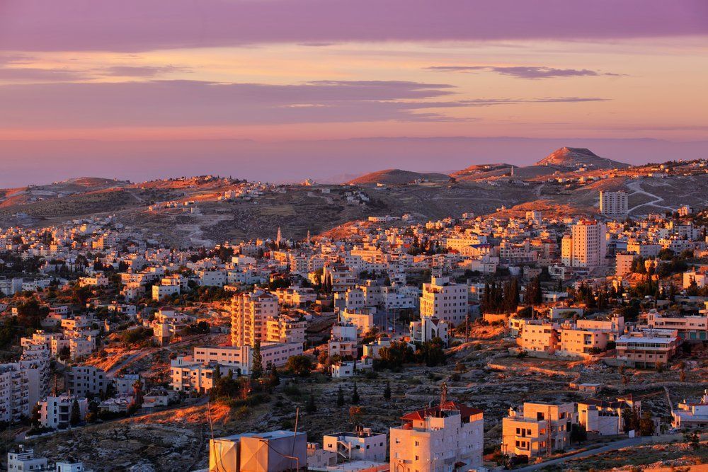 Sunset over a dense cityscape with white buildings and hills in warm orange and purple light