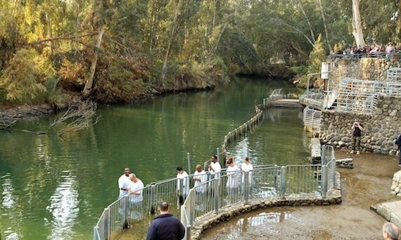 People standing by a fenced path beside a green river in a wooded park