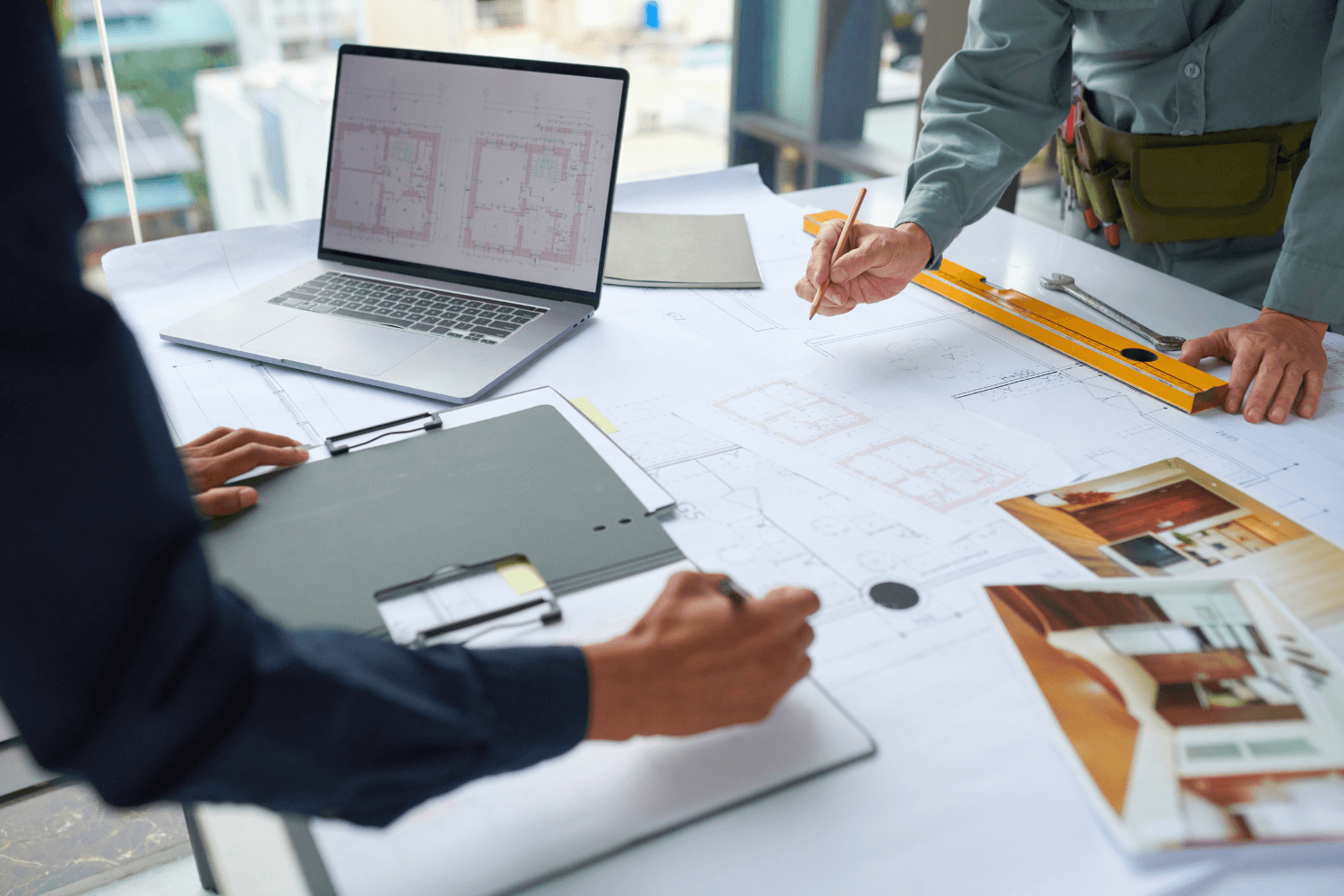 Personas trabajando en planos y un ordenador portátil en una mesa.