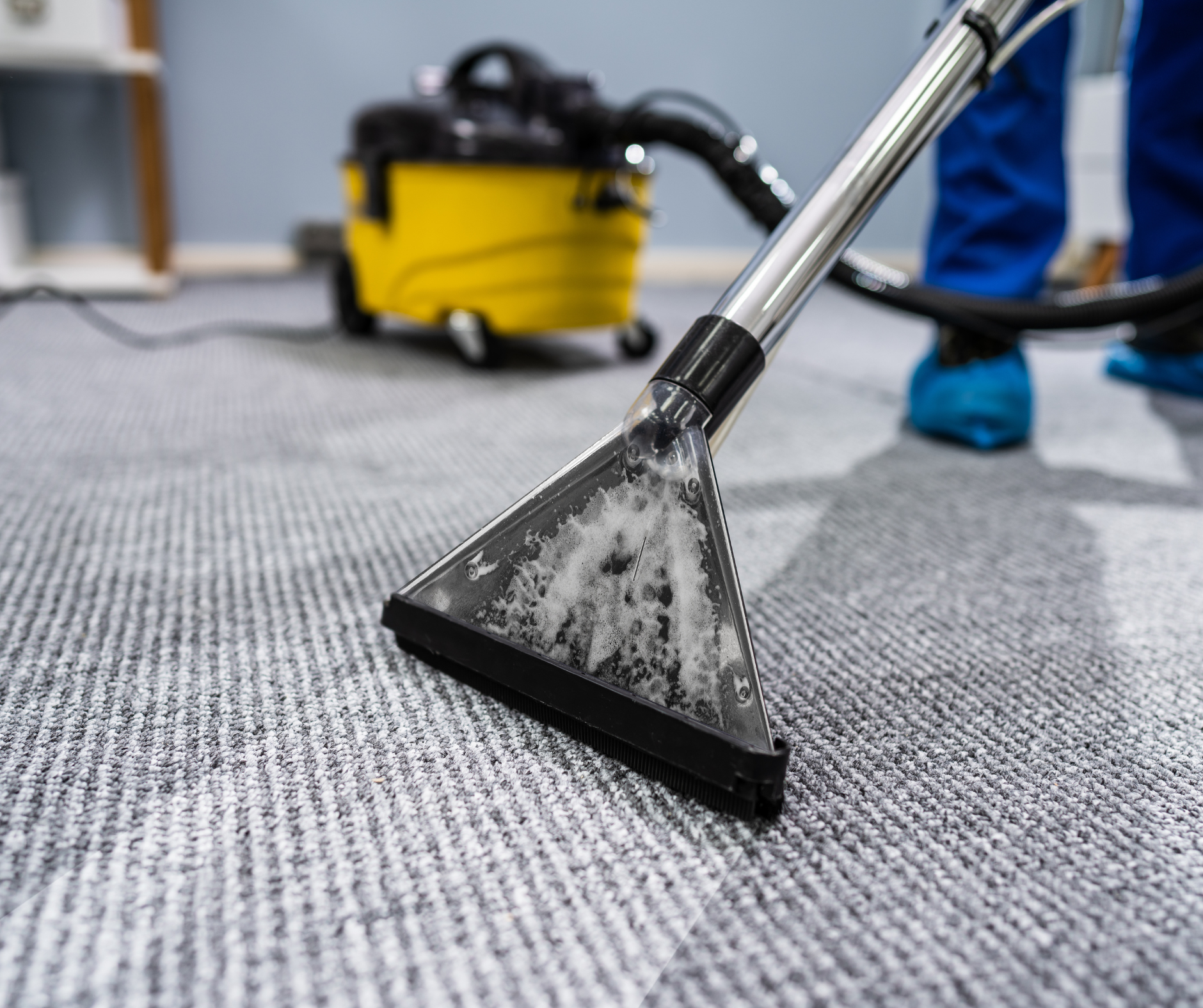 Person vacuuming gray carpet with a yellow professional cleaner in a room.