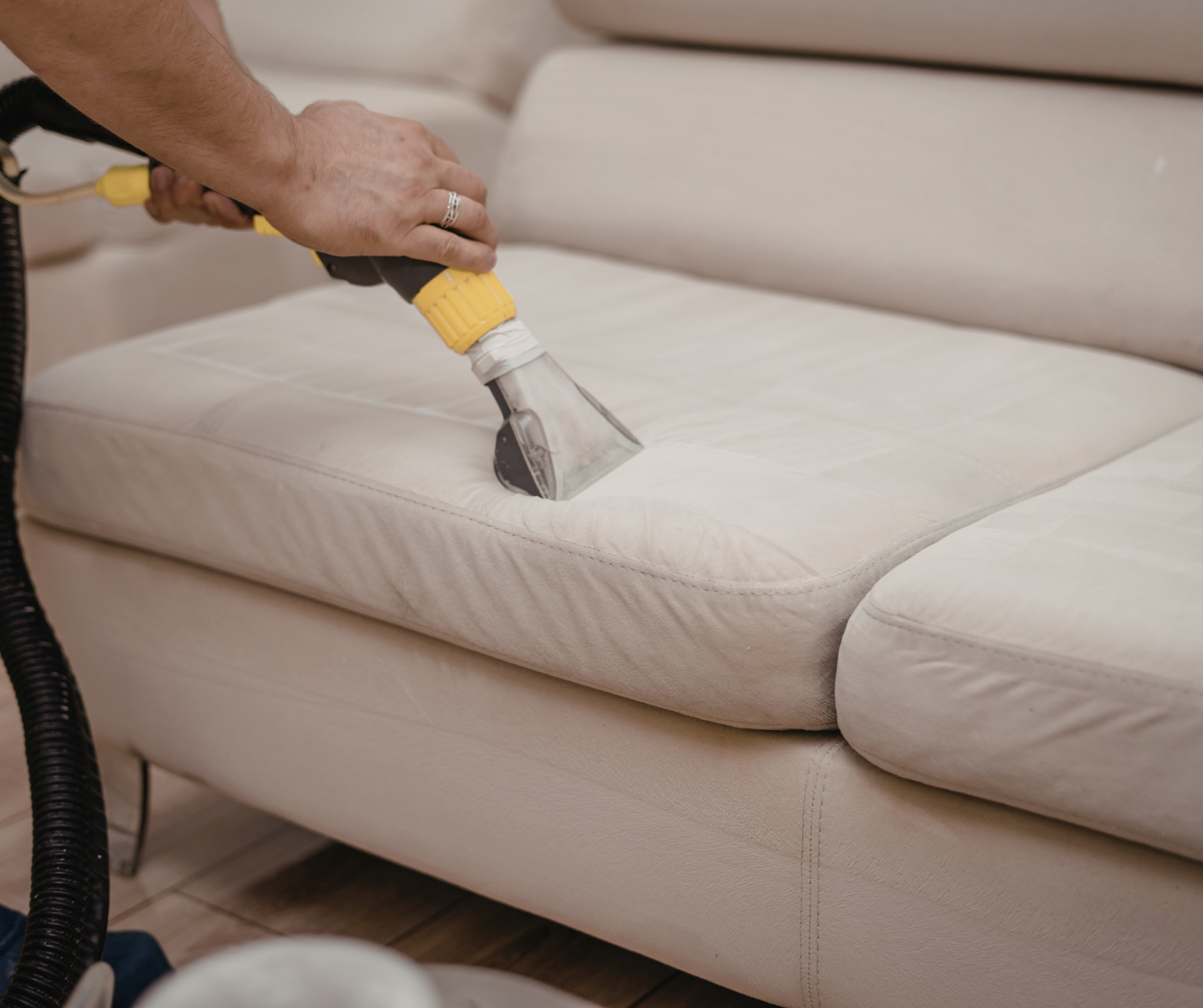 Person cleaning a beige sofa cushion with a handheld upholstery cleaner.