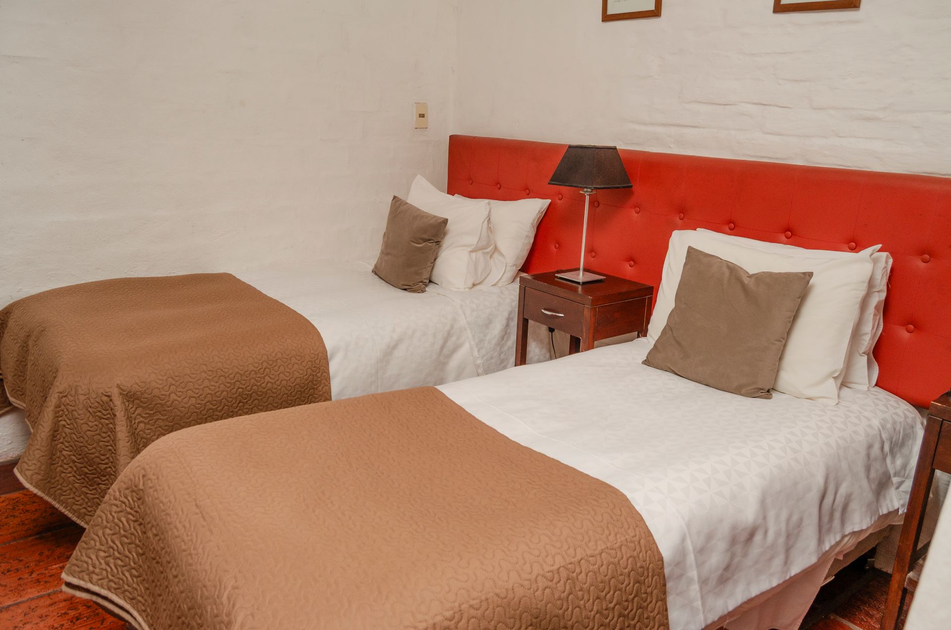 Una habitación de hotel con dos camas individuales con sábanas blancas, mantas marrones, cojines marrones y un cabecero acolchado de color naranja brillante.