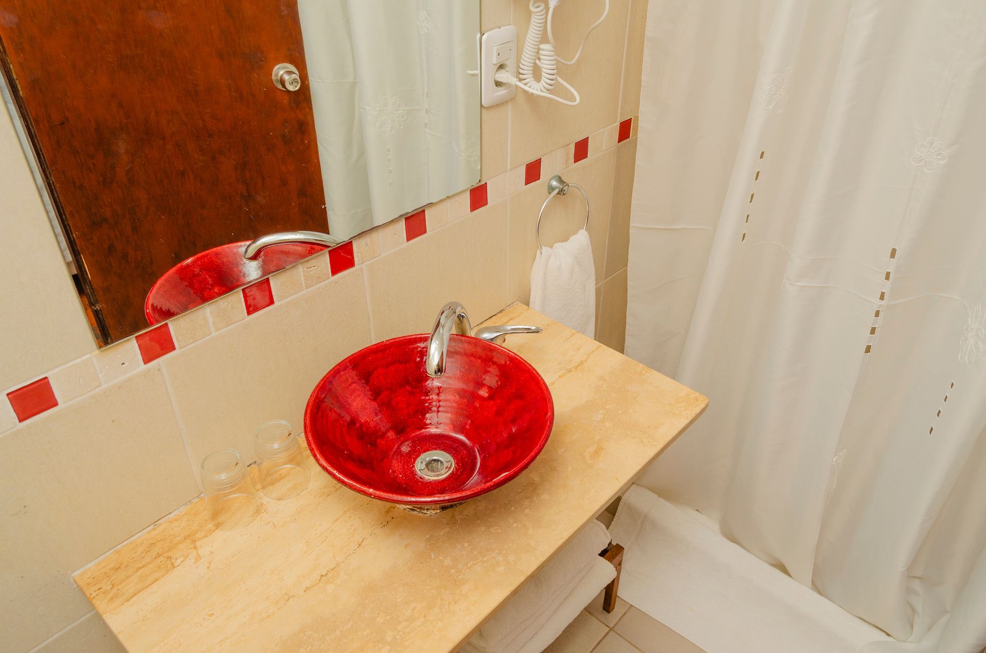 Un moderno mueble de baño con un lavabo circular de color rojo brillante sobre una encimera de madera clara con un protector contra salpicaduras de azulejos.