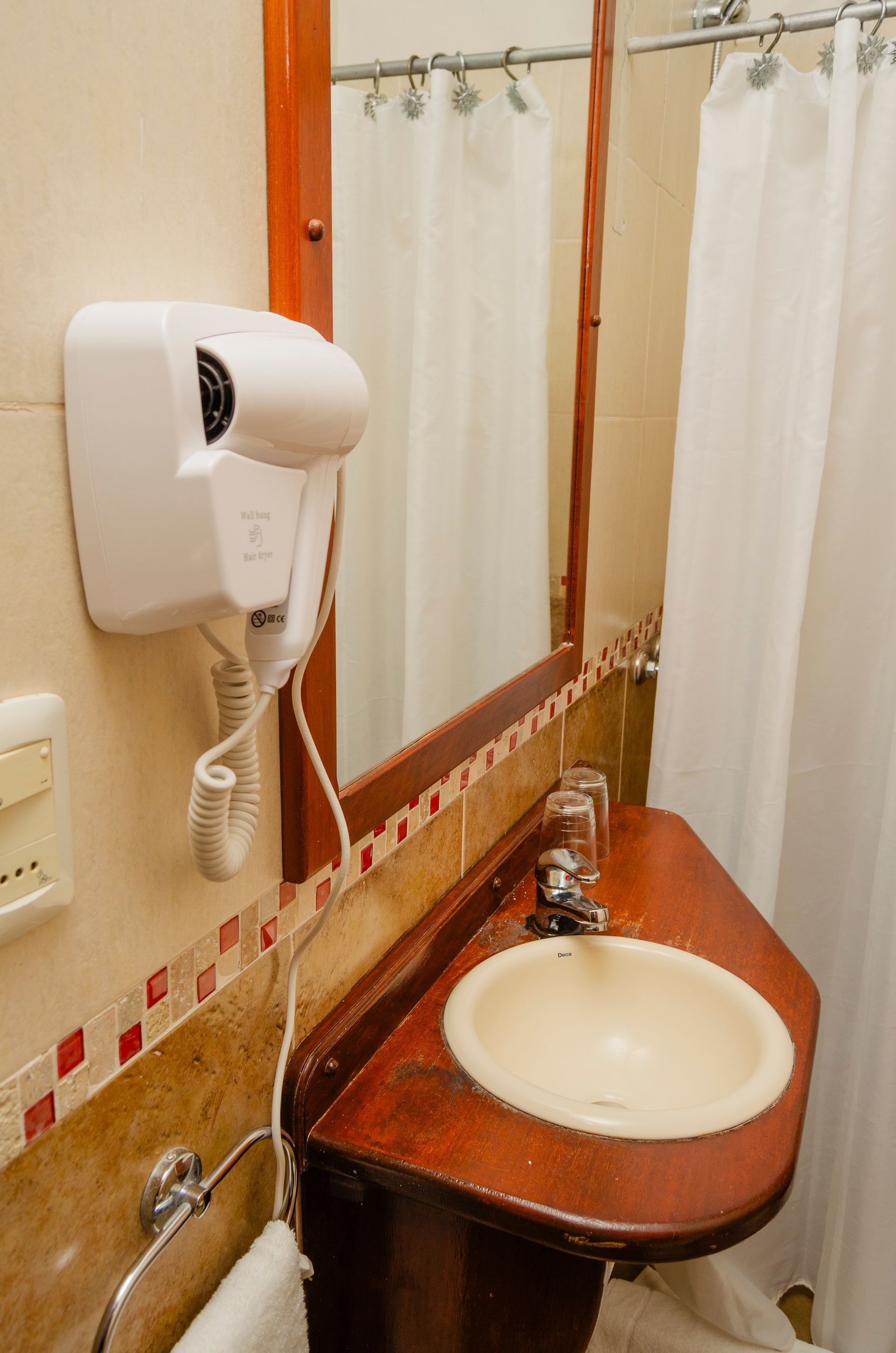 Un tocador de baño de hotel con un secador de pelo blanco montado en la pared, un espejo y un lavabo integrado en una encimera de madera.