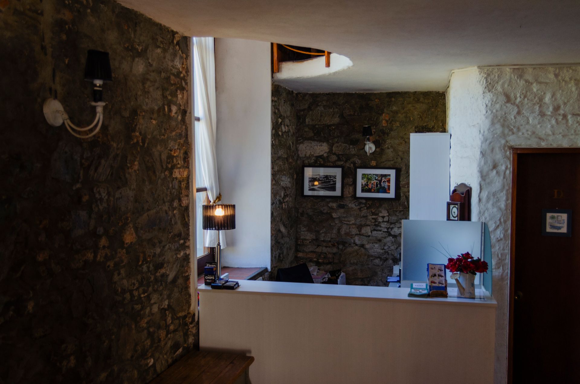 La recepción de un hotel tiene paredes de piedra, lámparas decorativas, cuadros enmarcados y un mostrador.