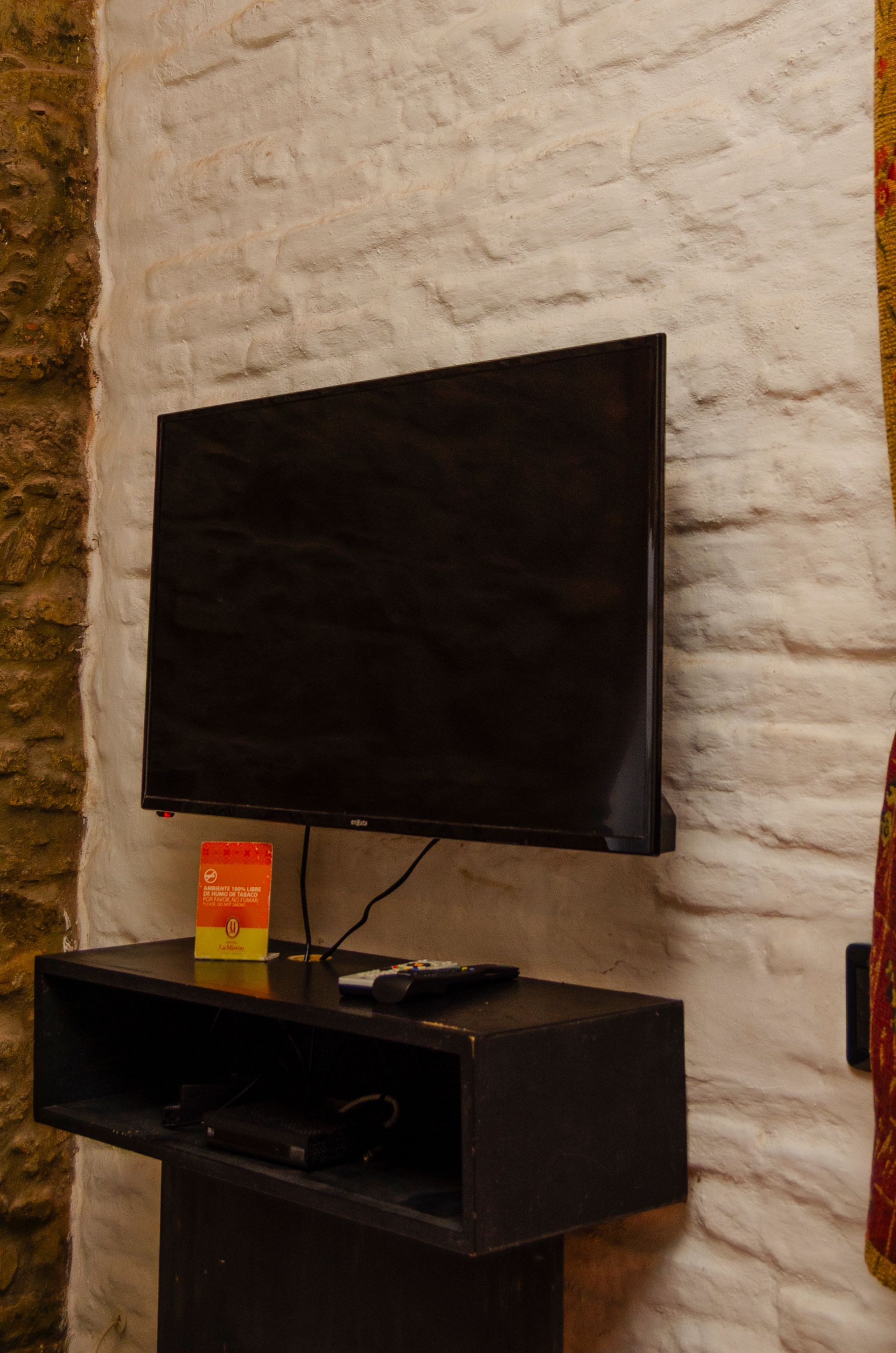 Un televisor de pantalla plana montado en una pared de ladrillo blanco, encima de un pequeño mueble negro para equipos multimedia.