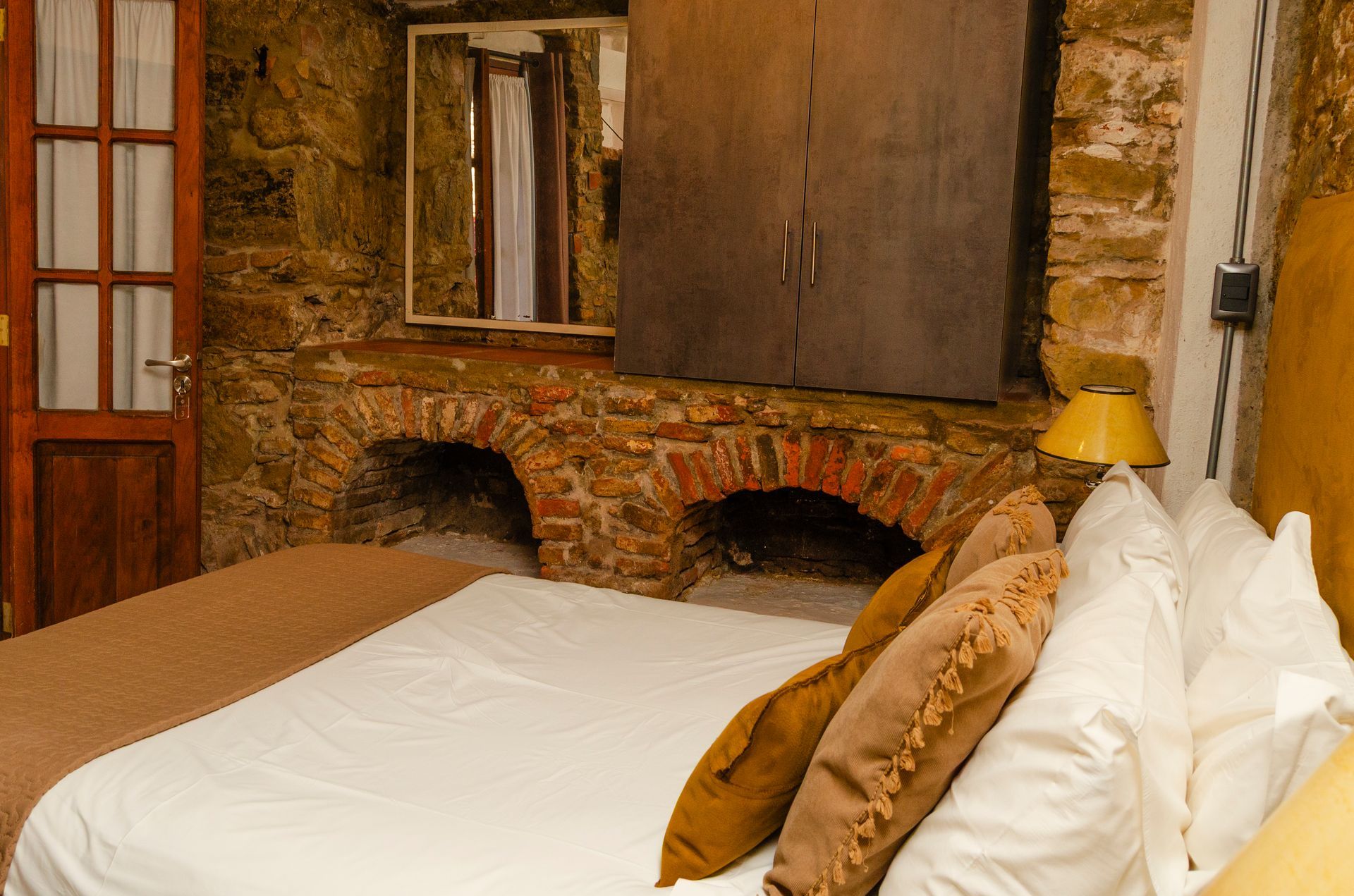 Un dormitorio rústico cuenta con una cama con sábanas y almohadas blancas, situada contra una pared de piedra con dos nichos arqueados.