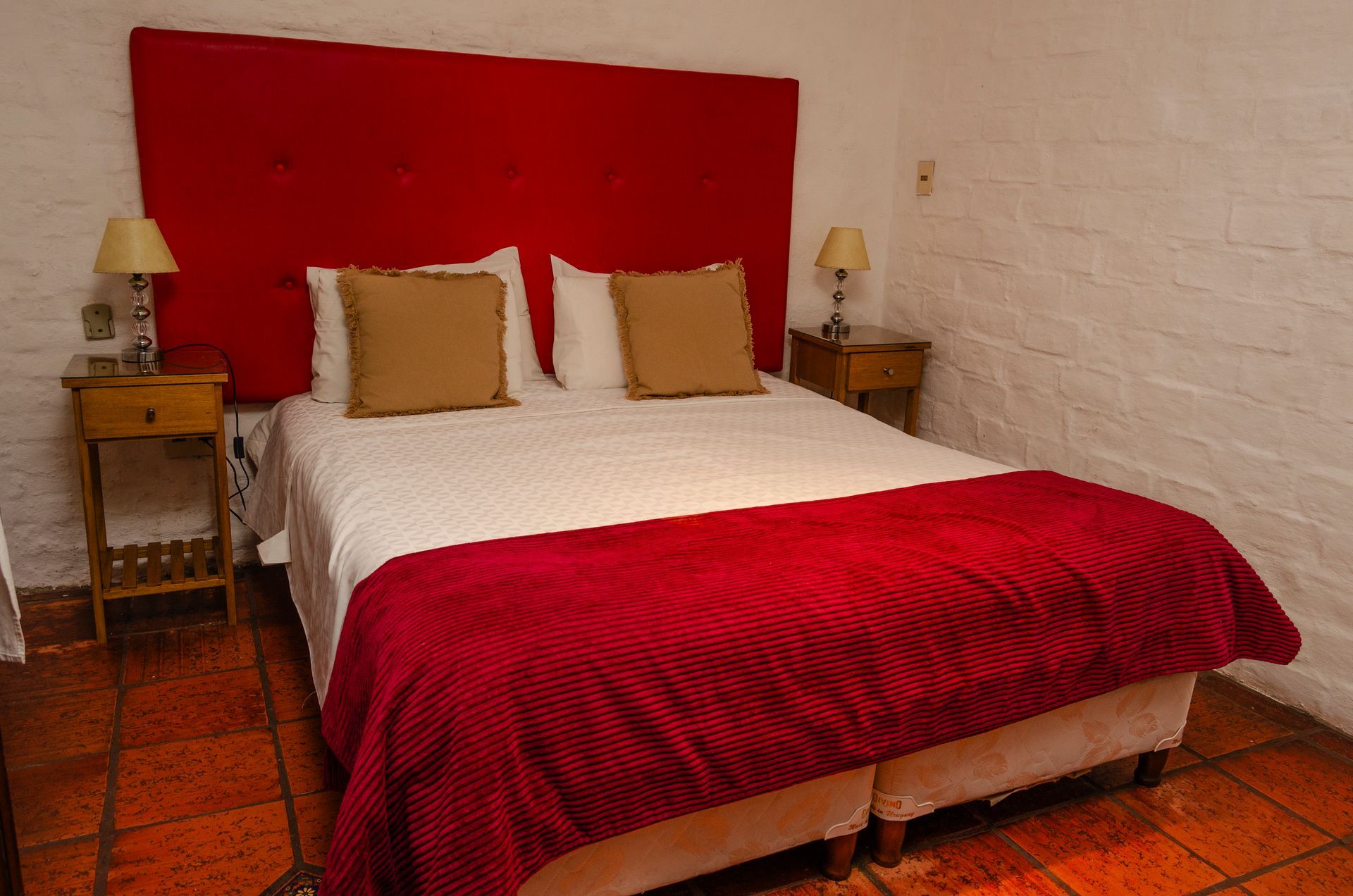 Un dormitorio con una cama que cuenta con un cabecero rojo y una colcha roja a juego, flanqueada por dos mesitas de noche de madera con lámparas.
