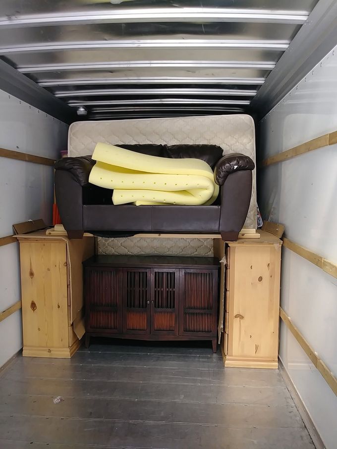 Furniture strapped inside a moving truck, with boxes and a couch secured against the front wall.
