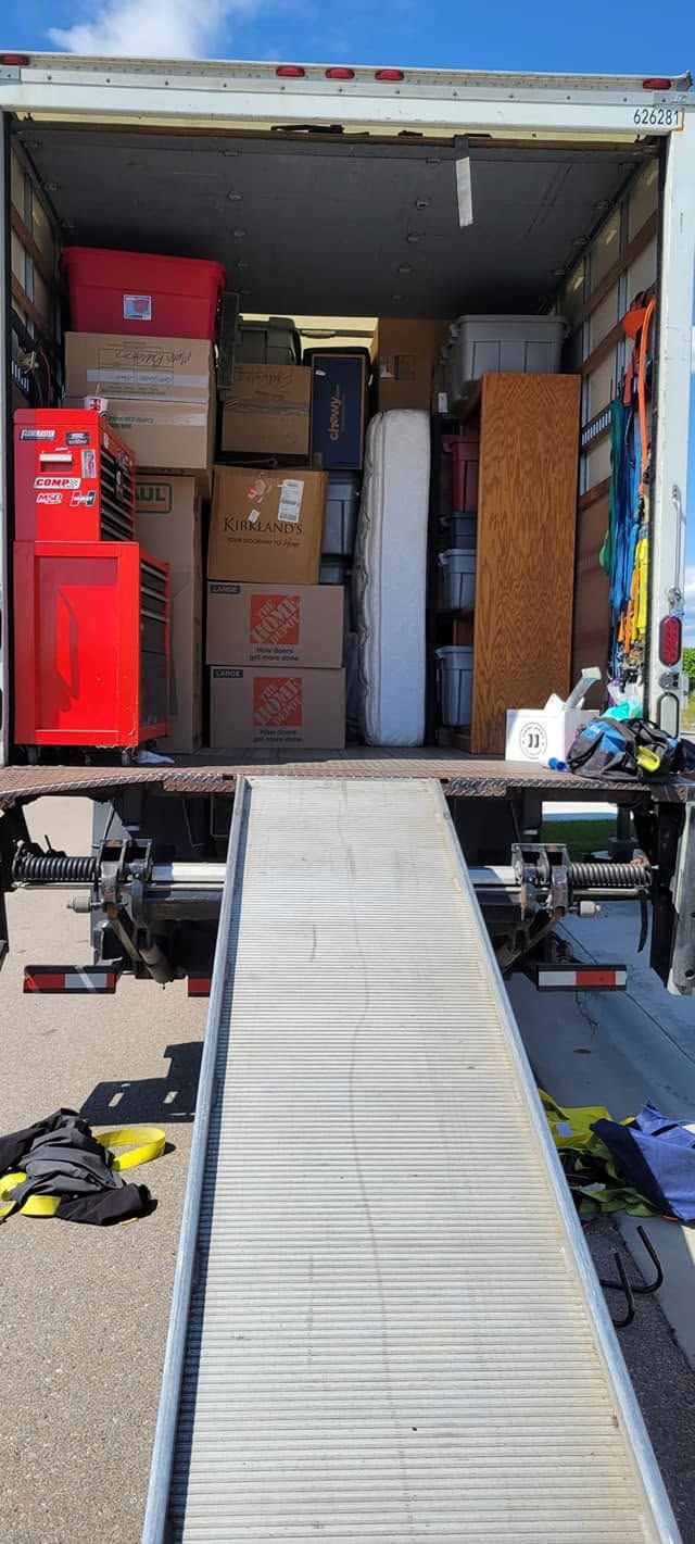 Moving truck with open cargo bay and ramp, packed with stacked boxes and furniture.