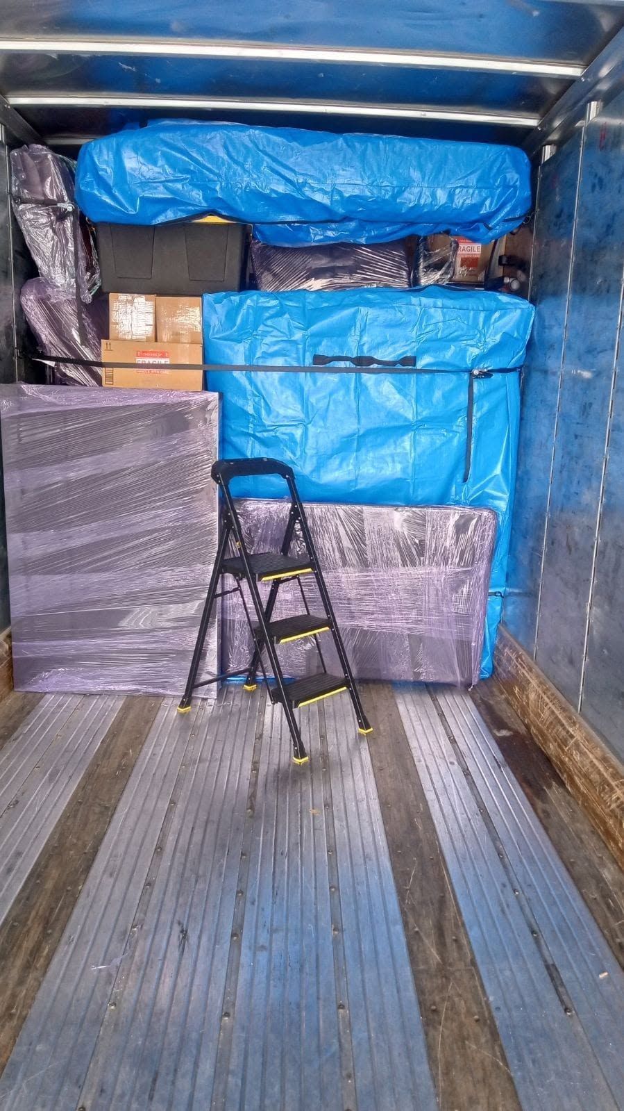 Ladder inside a moving truck, with blue tarps and stacked boxes securing cargo.