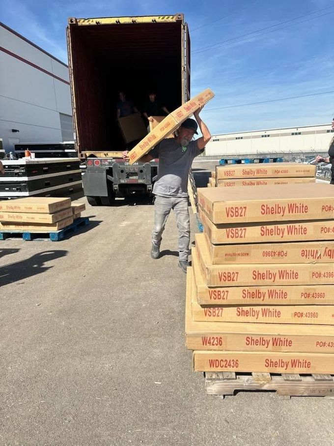 Worker loading stacked cardboard boxes into a truck on a sunny loading dock
