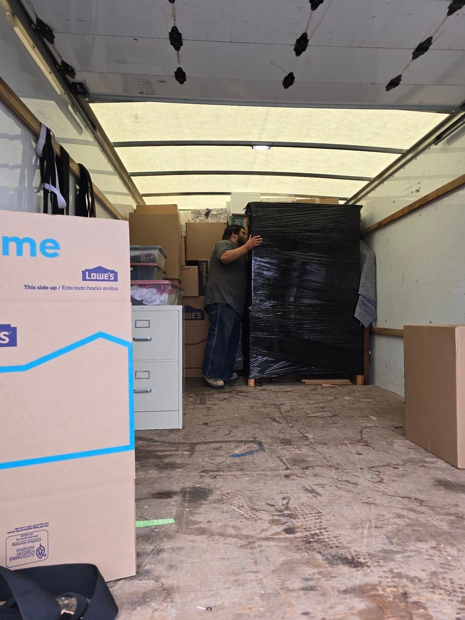 Person loading a truck with cardboard boxes and a large black-wrapped item.