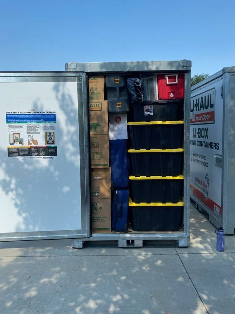 Open utility storage box with shelves, equipment, and a red compartment on a sidewalk outdoors