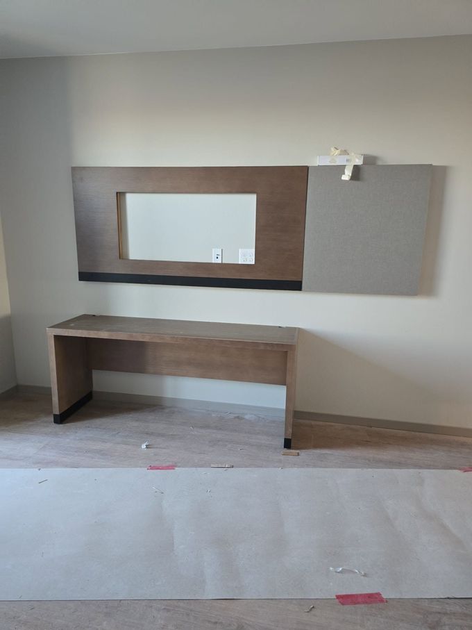 Empty room with built-in wooden desk and wall mirror mounted on a gray panel wall.