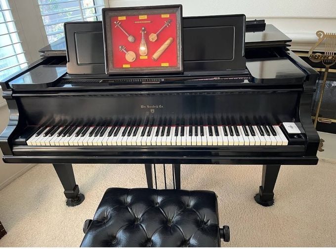 Black grand piano with an open framed clock on the music stand and a tufted bench in front