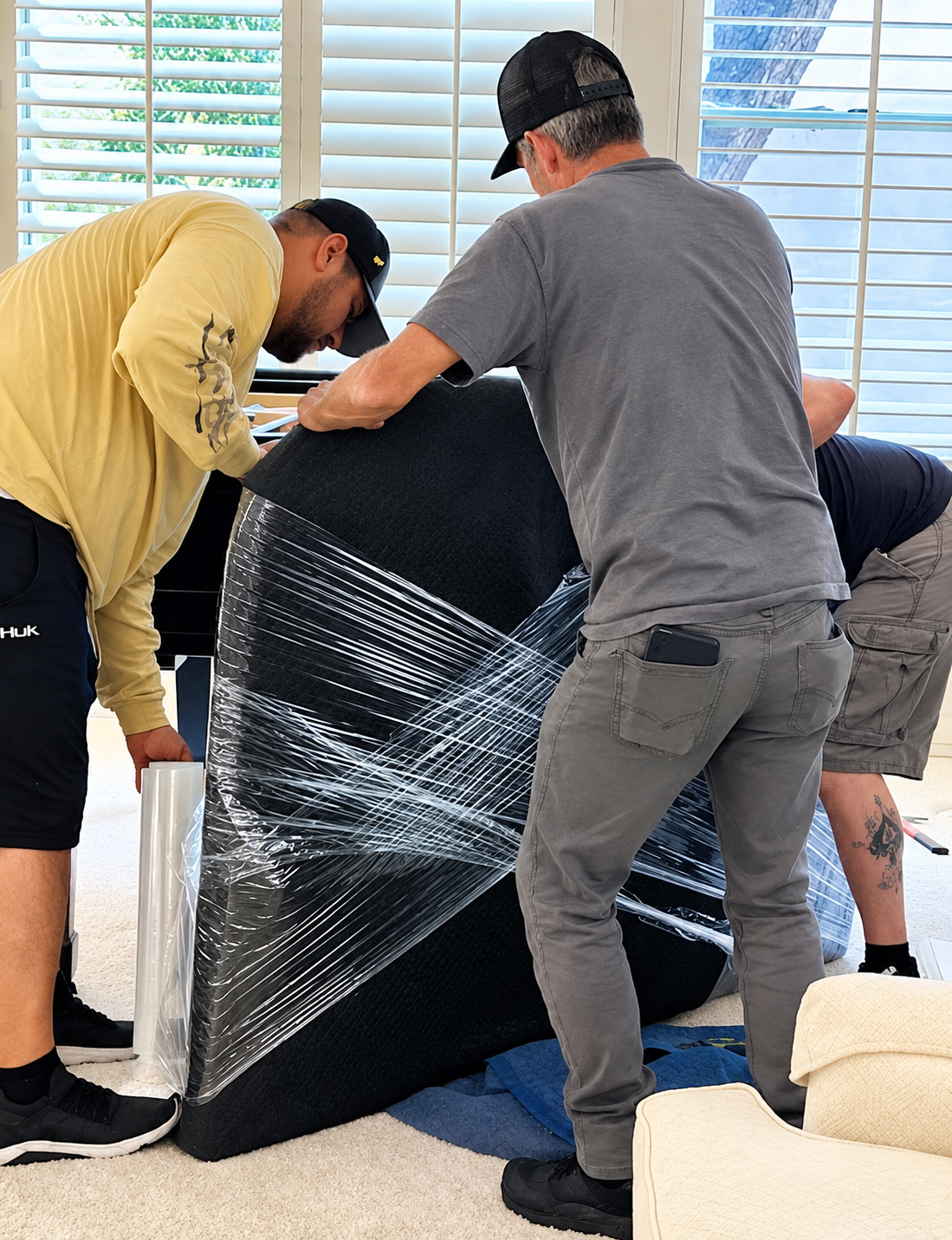 Several people wrap a black couch in plastic while moving it indoors.