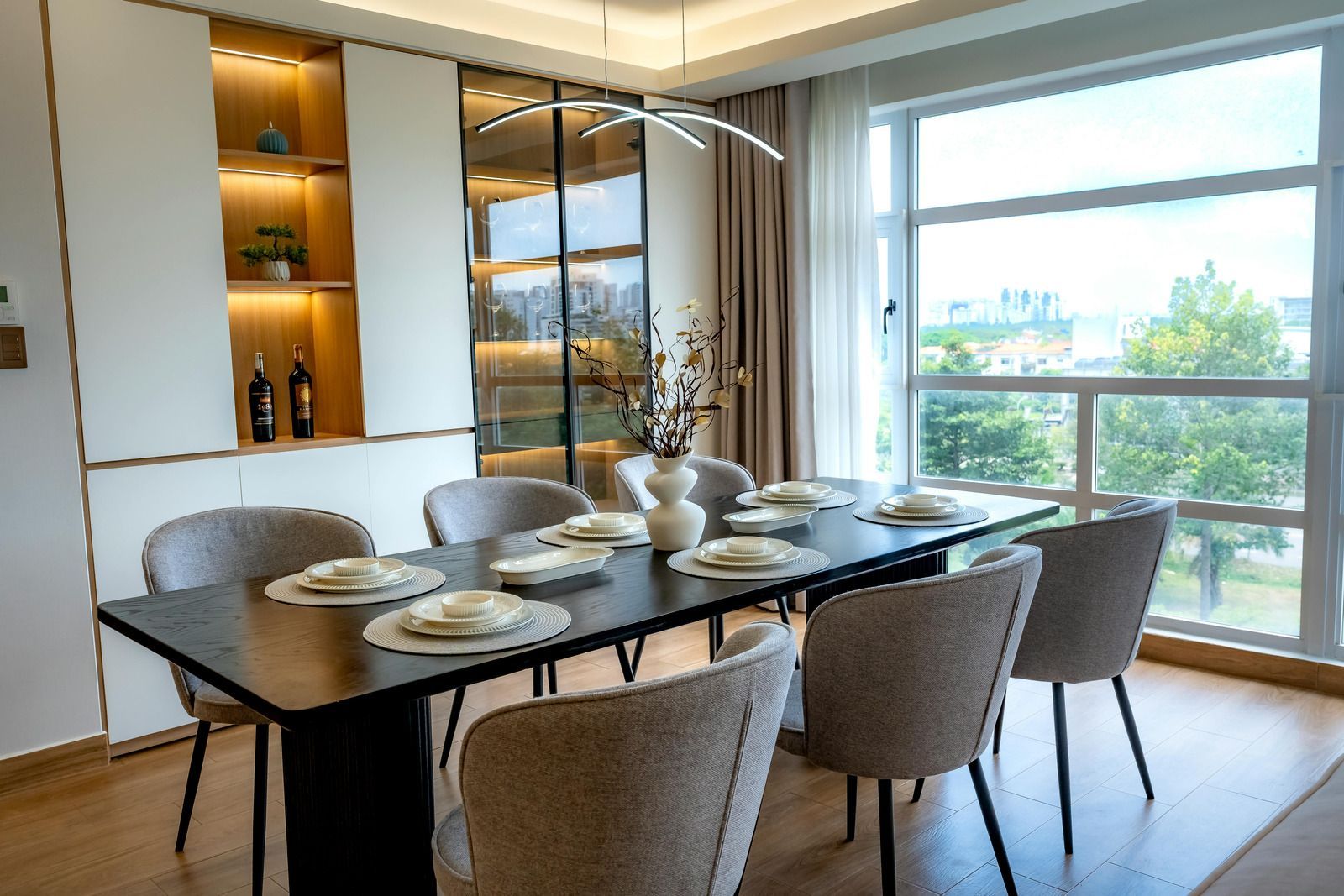 Modern dining room with a glass table set for six beside a large window overlooking greenery