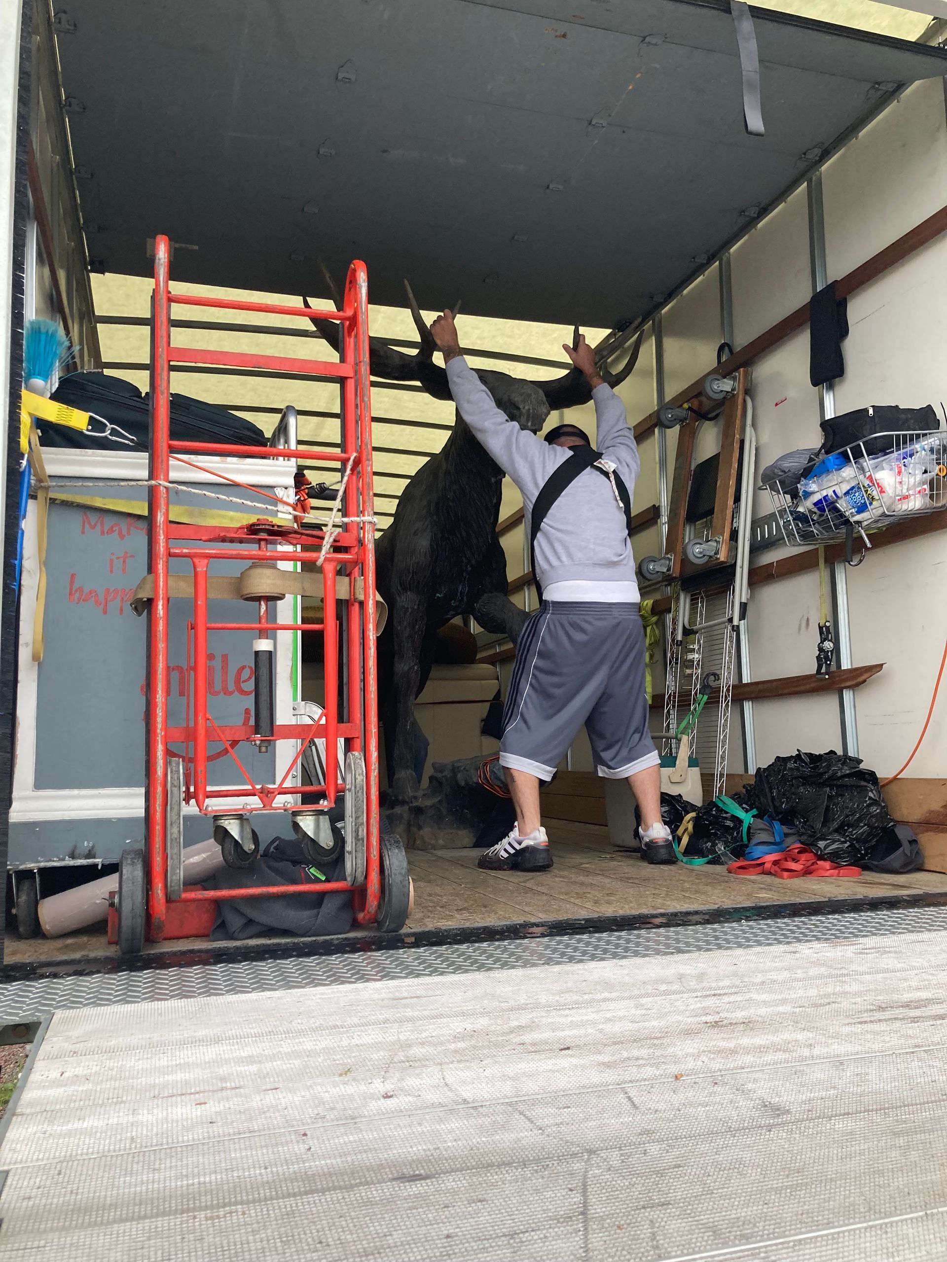 Person reaching up inside a van with shelves and a red ladder, surrounded by tools and equipment.