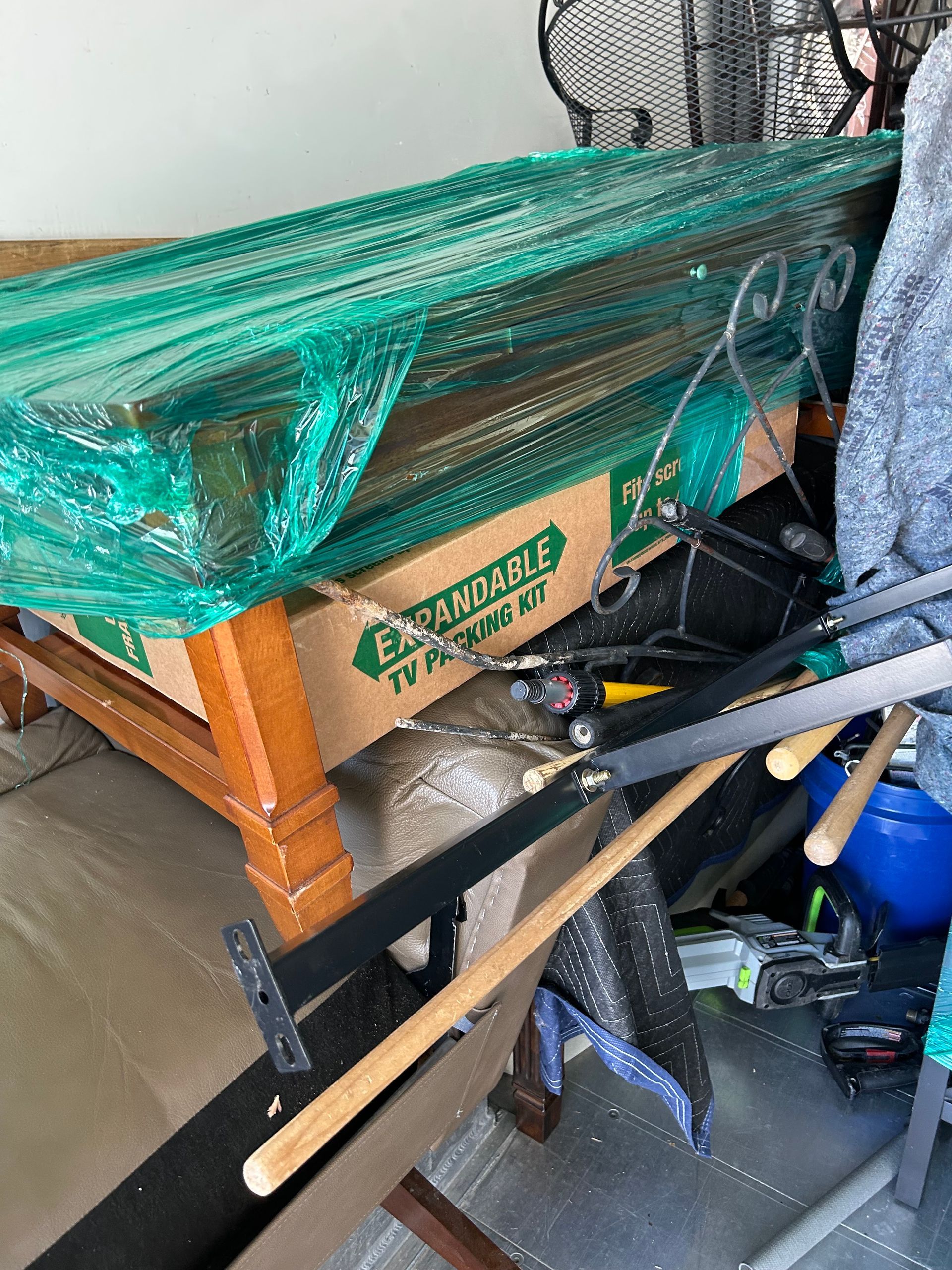 Cluttered storage area with a wooden table, green netting, tools, and cardboard boxes piled together.