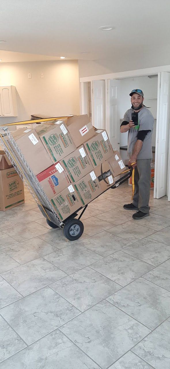 Man pushing a large taped cardboard box on a hand truck in a lobby with tile floors