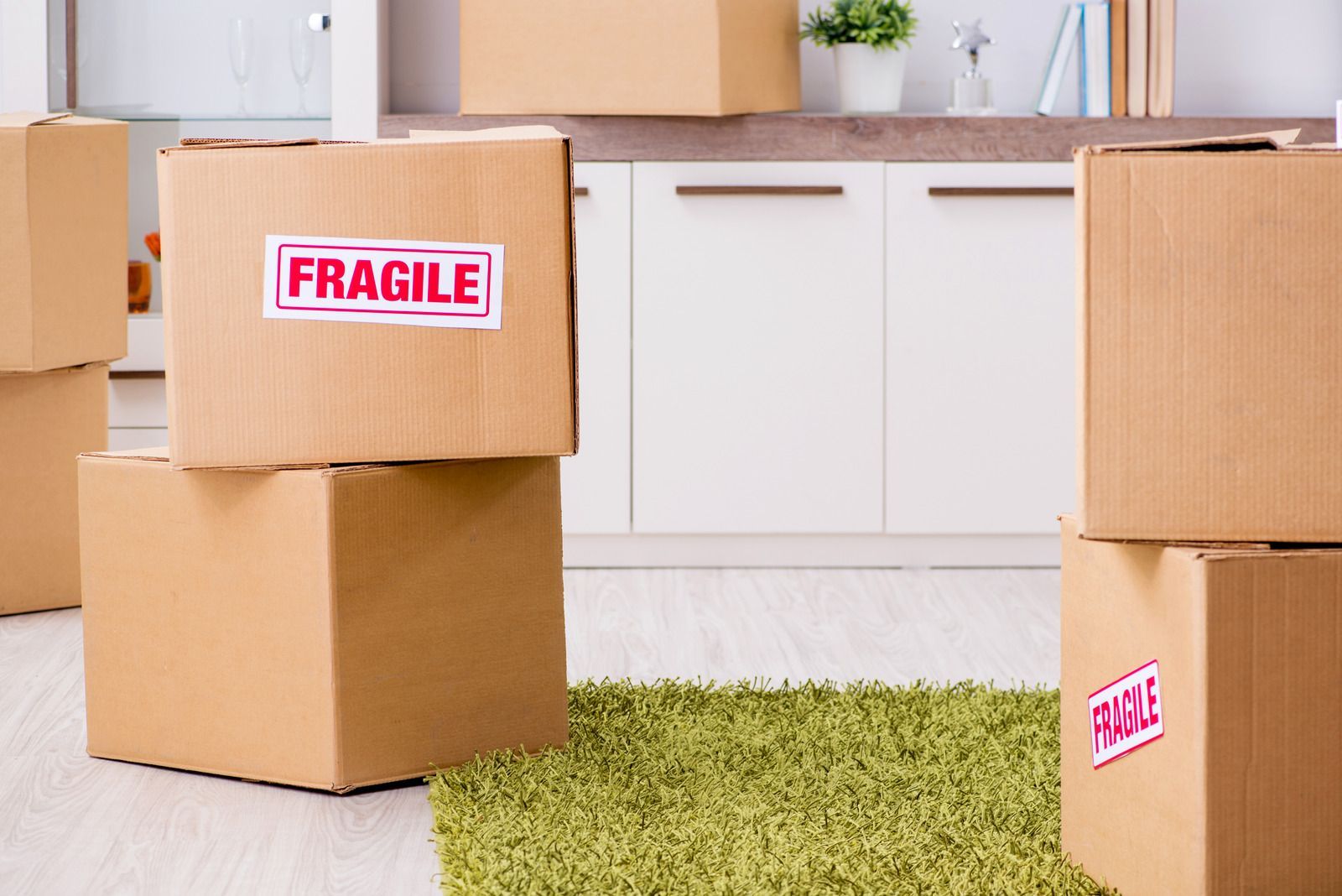 Cardboard moving boxes labeled “FRAGILE” stacked in a bright room with a green rug.