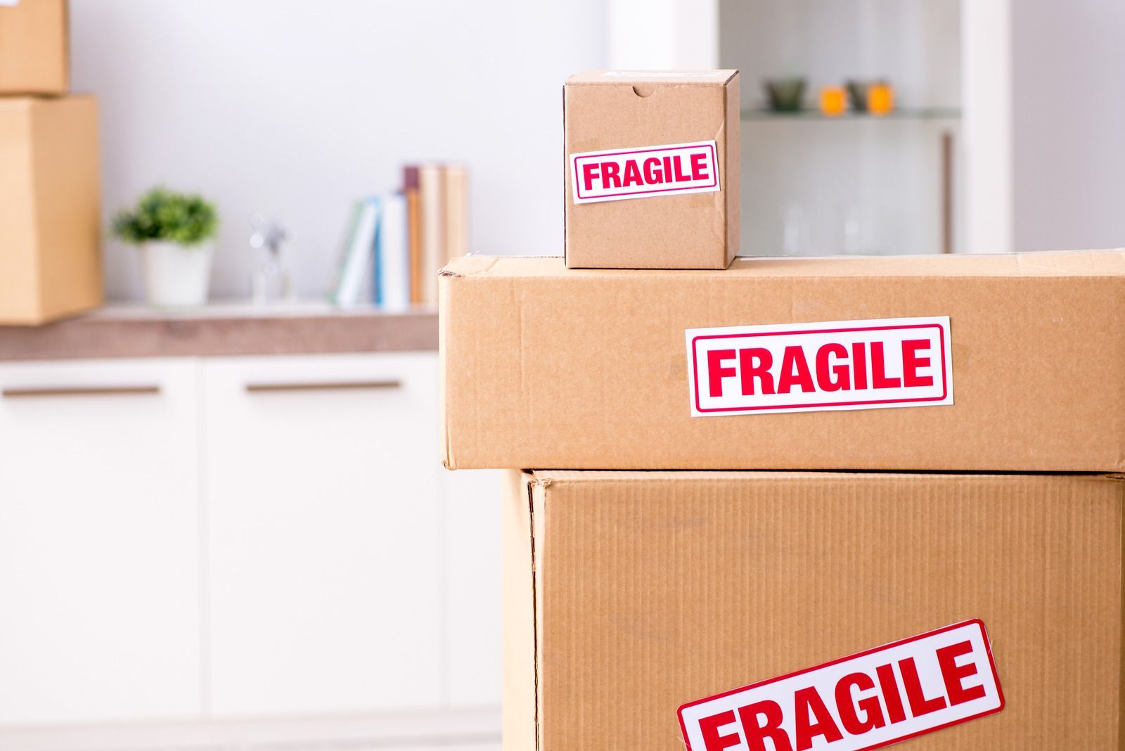 Stacked cardboard moving boxes labeled “FRAGILE” in a bright kitchen/room