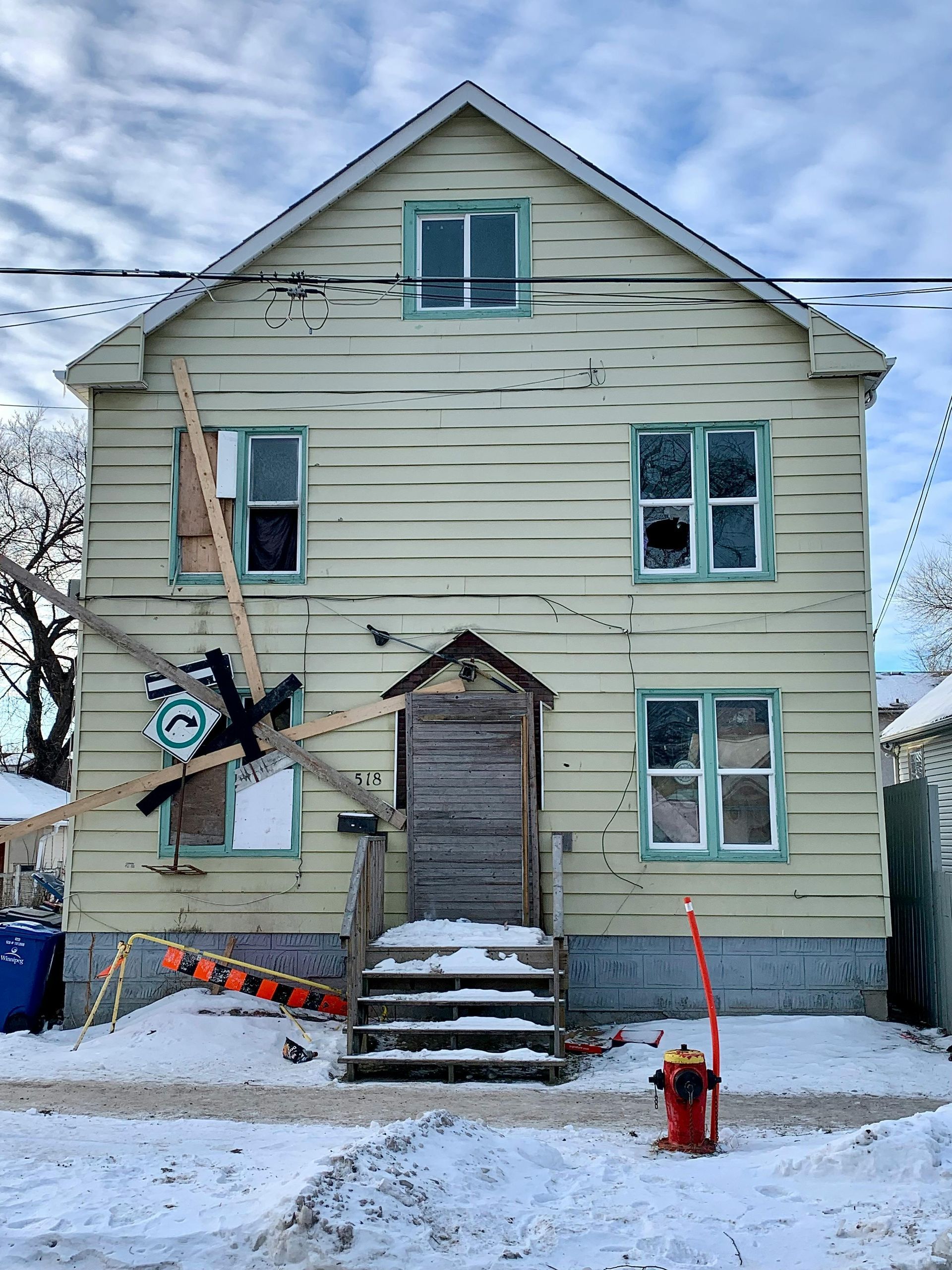 Damaged two-story house with broken window, debris, and snow on the ground, likely after impact.