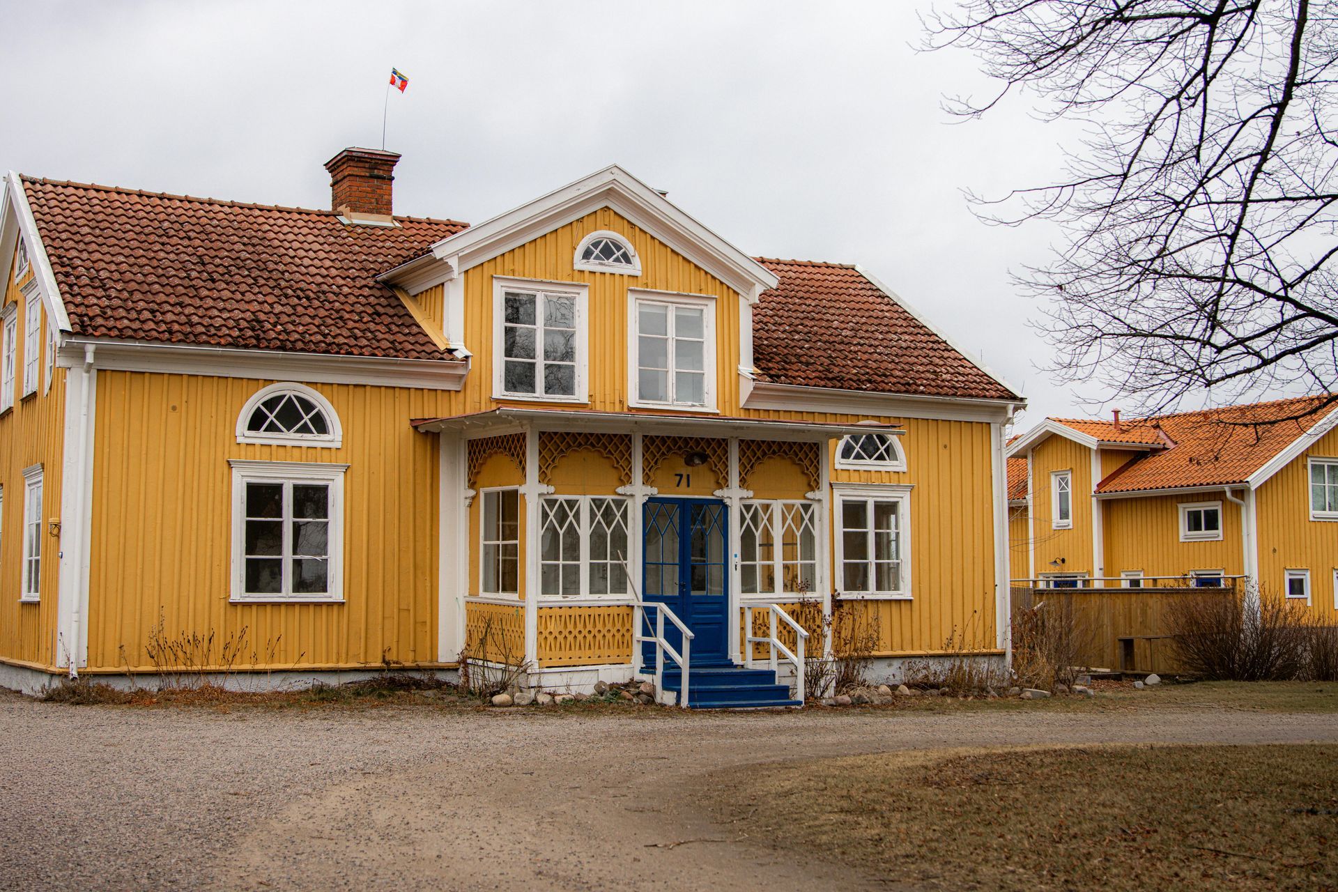 Yellow wooden house with blue front steps and white trim on a quiet street under cloudy sky