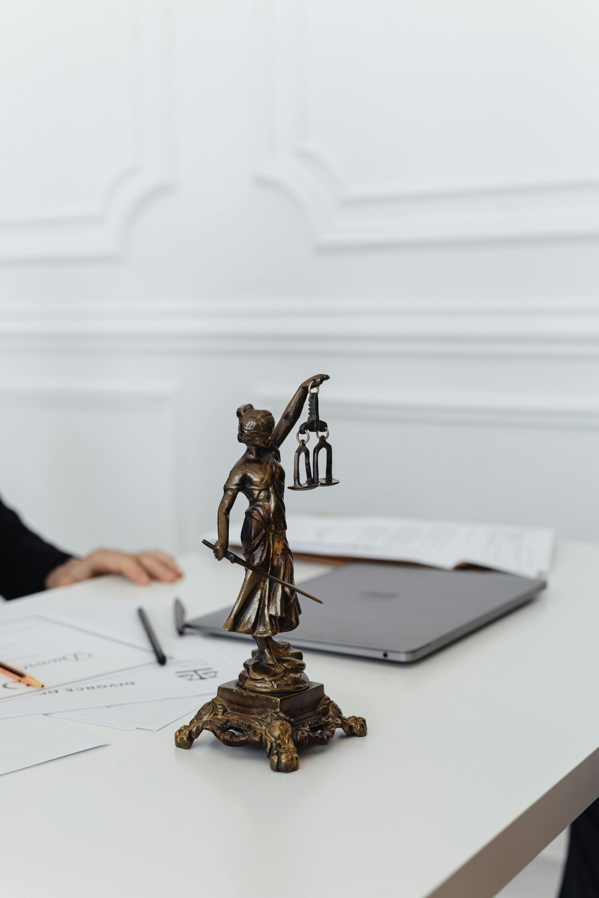 Statue of Lady Justice holding a lantern, next to a laptop on a white table with documents.