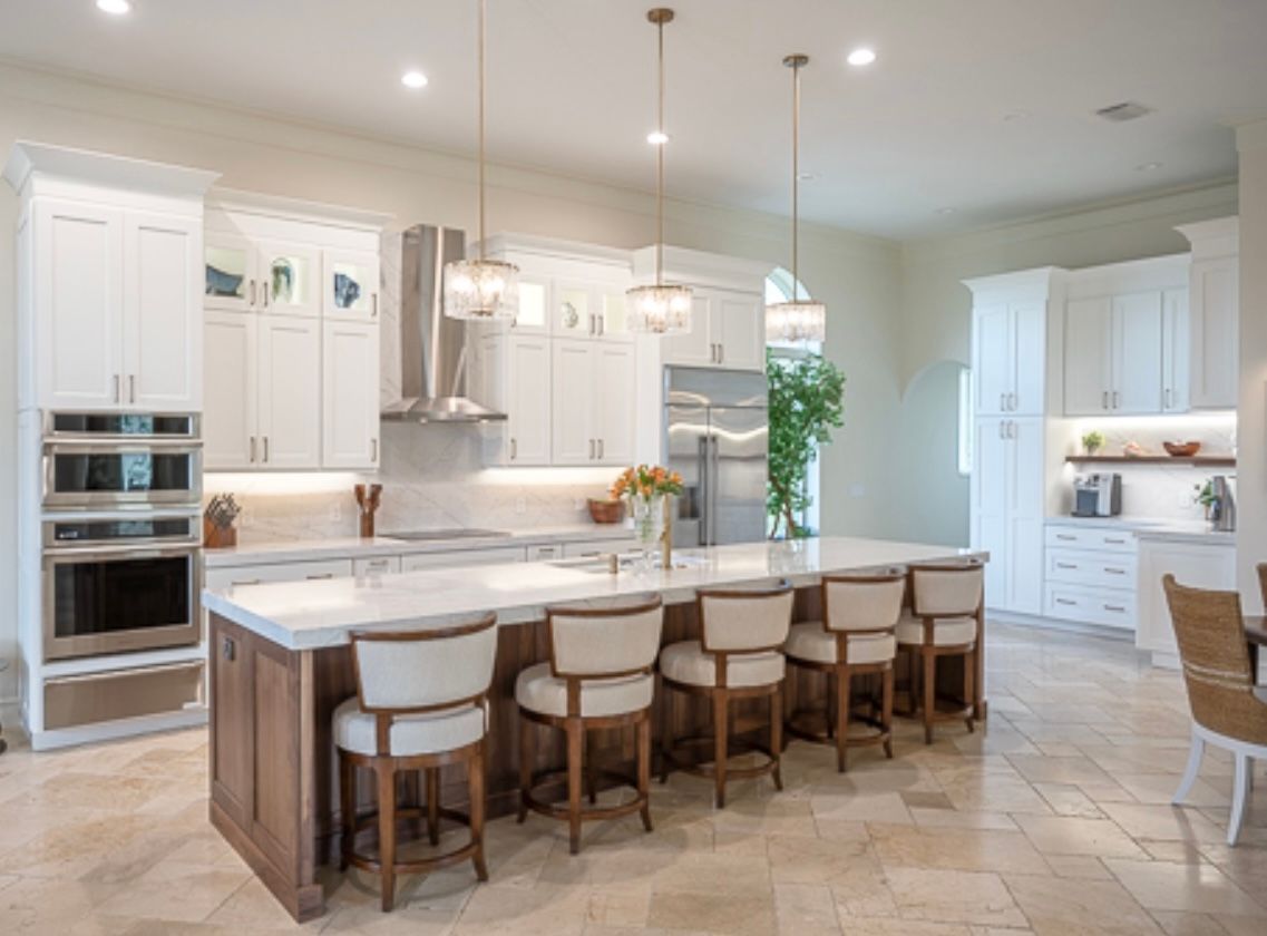 Bright white modern kitchen with large island, pendant lights, and wood stools, viewed into an open dining area at CRAFTED 1111 fashion