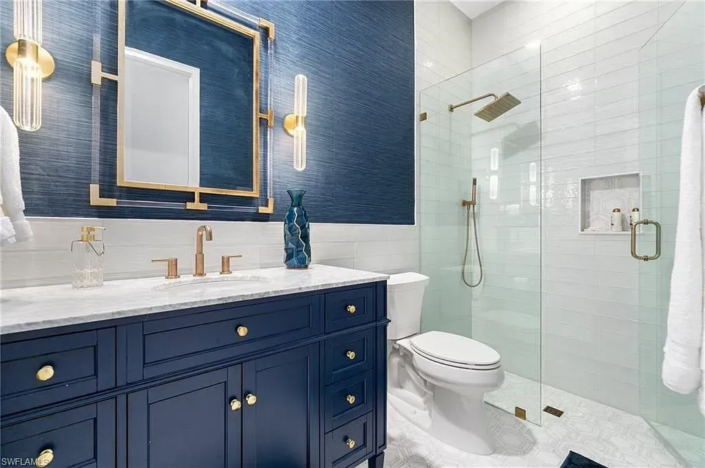 Elegant blue-and-gold bathroom with white tile, double vanity, mirror, and glass shower enclosure at CRAFTED 1111 fashion