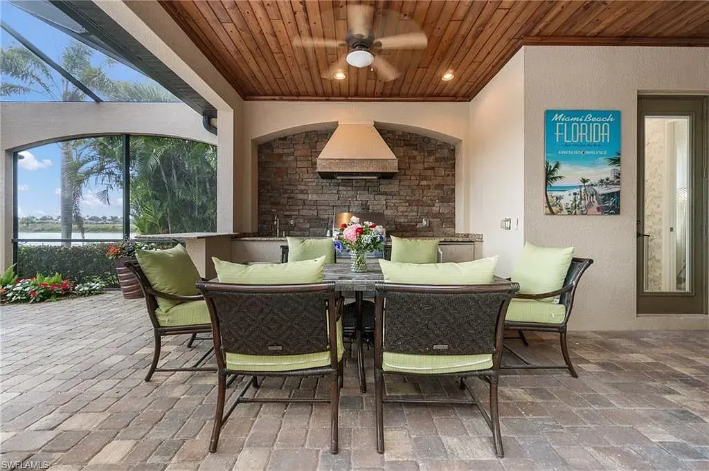 Covered patio with wicker dining set, stone fireplace, ceiling fan, and lake view through large opening at CRAFTED 1111 fashion