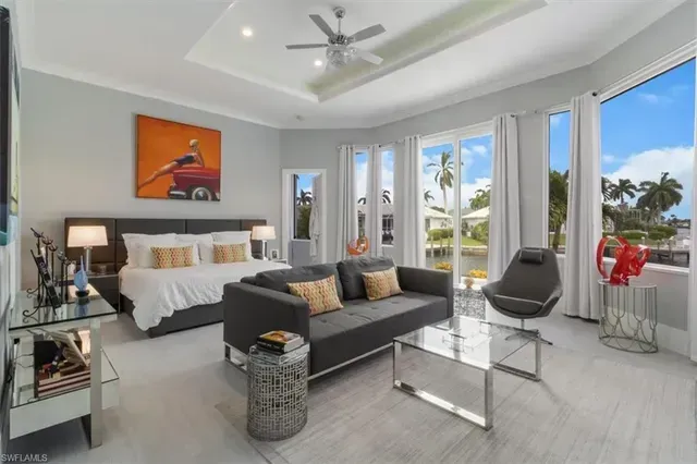 Bright modern bedroom with white bed, gray sofa, glass table, and bay windows overlooking palm trees at CRAFTED 1111 fashion