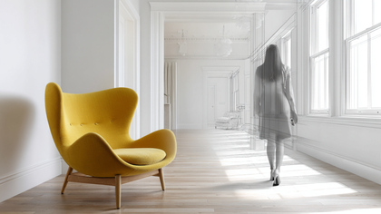 Yellow armchair in a bright white room, with a blurred figure walking near the windows Owners of Crafted 1111 standing outside a Florida home