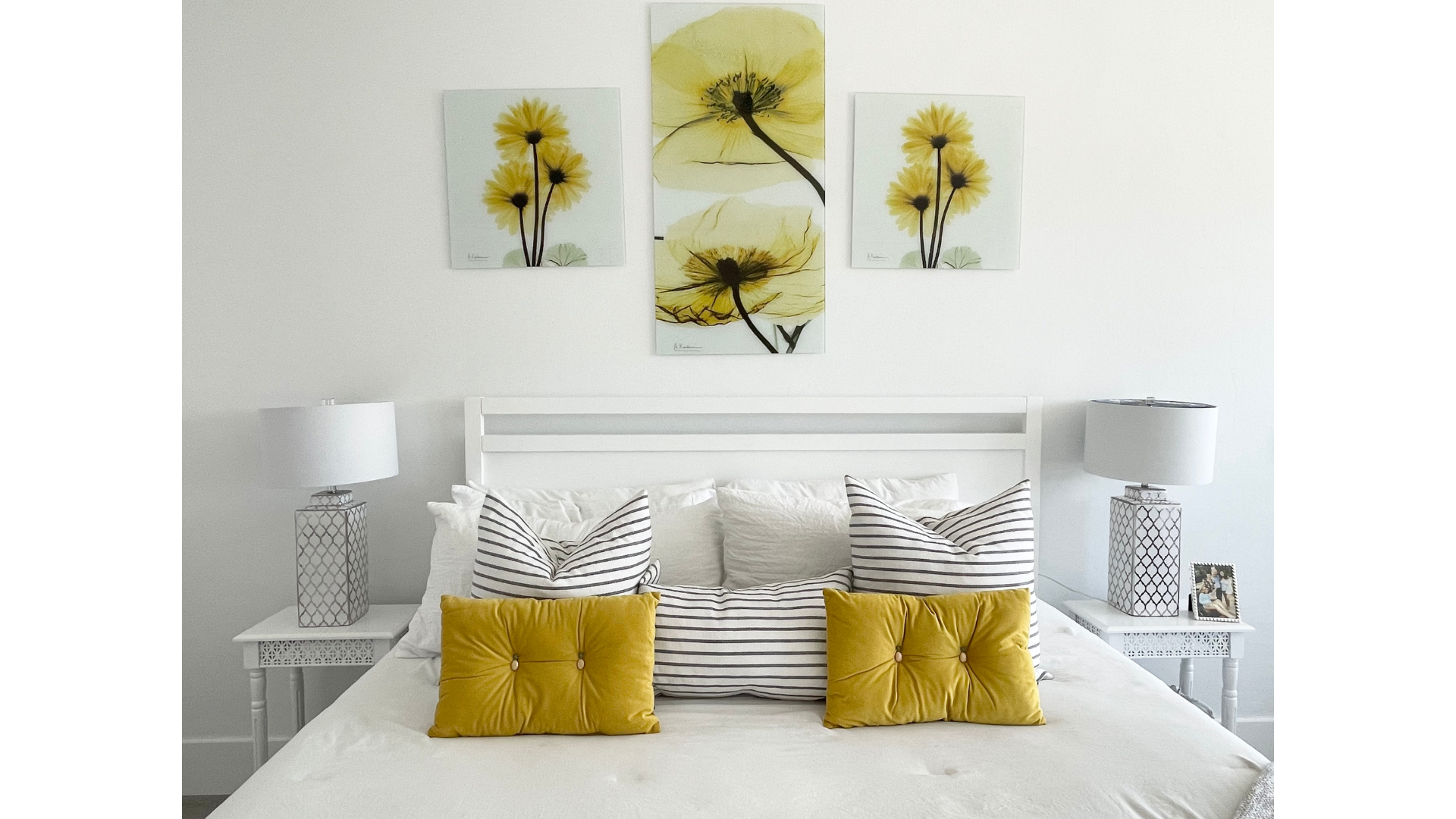 Bright white bedroom with yellow flower wall art, striped pillows, and mustard accent cushions on the bed at CRAFTED 1111 fashion