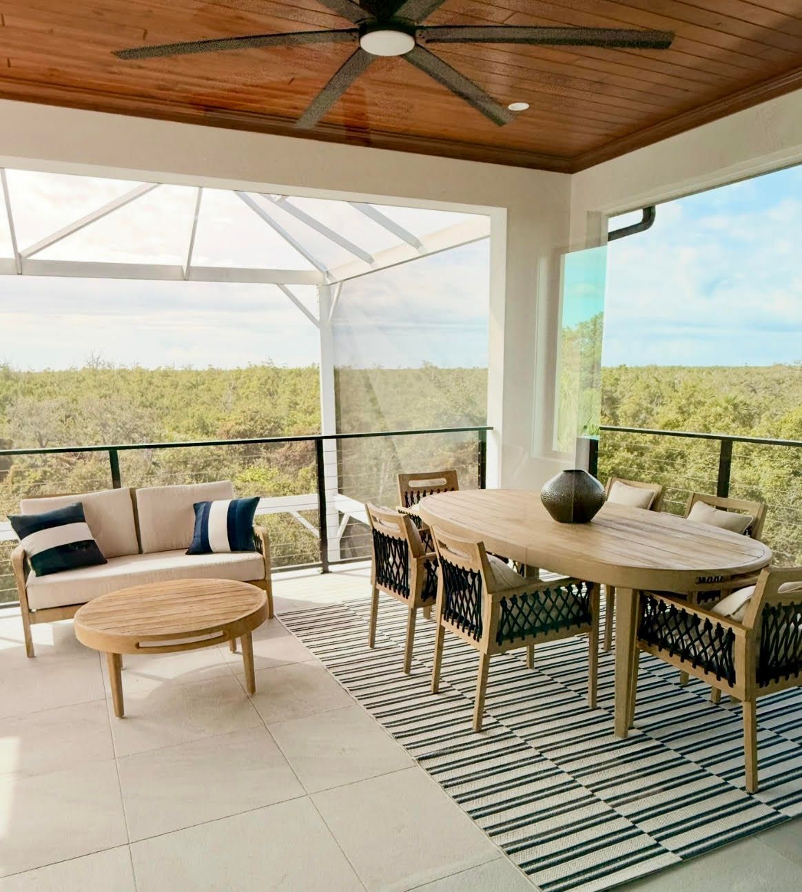 Covered patio with wicker seating, wooden dining table, striped rug, and a view of green marshland at Crafted 1111