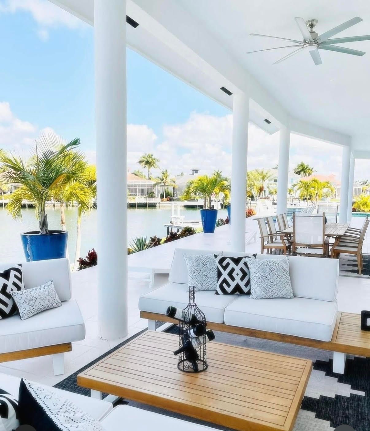 Bright white patio with wicker seating, palm trees, and blue sky overlooking water at CRAFTED 1111 fashion