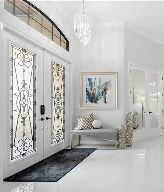 Elegant white entryway with ornate double doors, bench, chandelier, and abstract wall art at CRAFTED 1111 fashion
