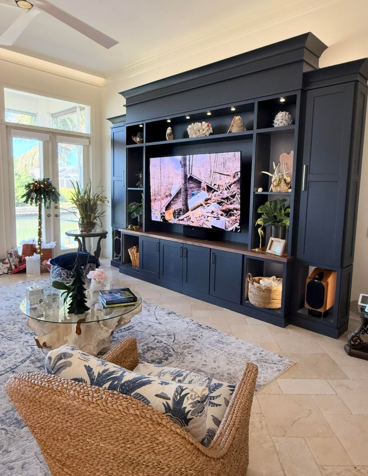 Modern living room with dark built-in media wall, TV, blue-patterned sofa, glass coffee table, and large windows at CRAFTED 1111 fashion