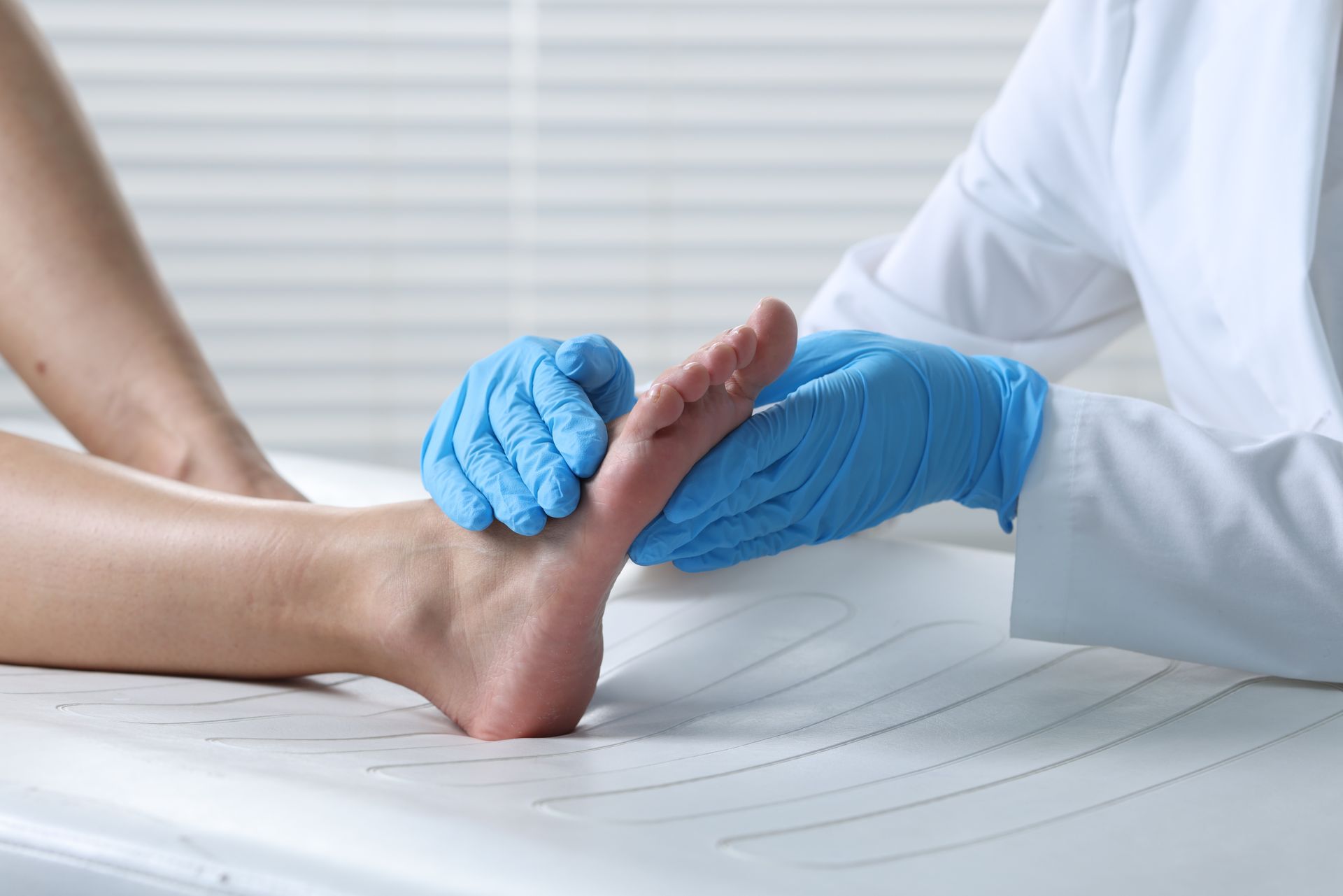 Doctor examining a patient's foot. Hands in blue gloves, white coat, on a medical table.